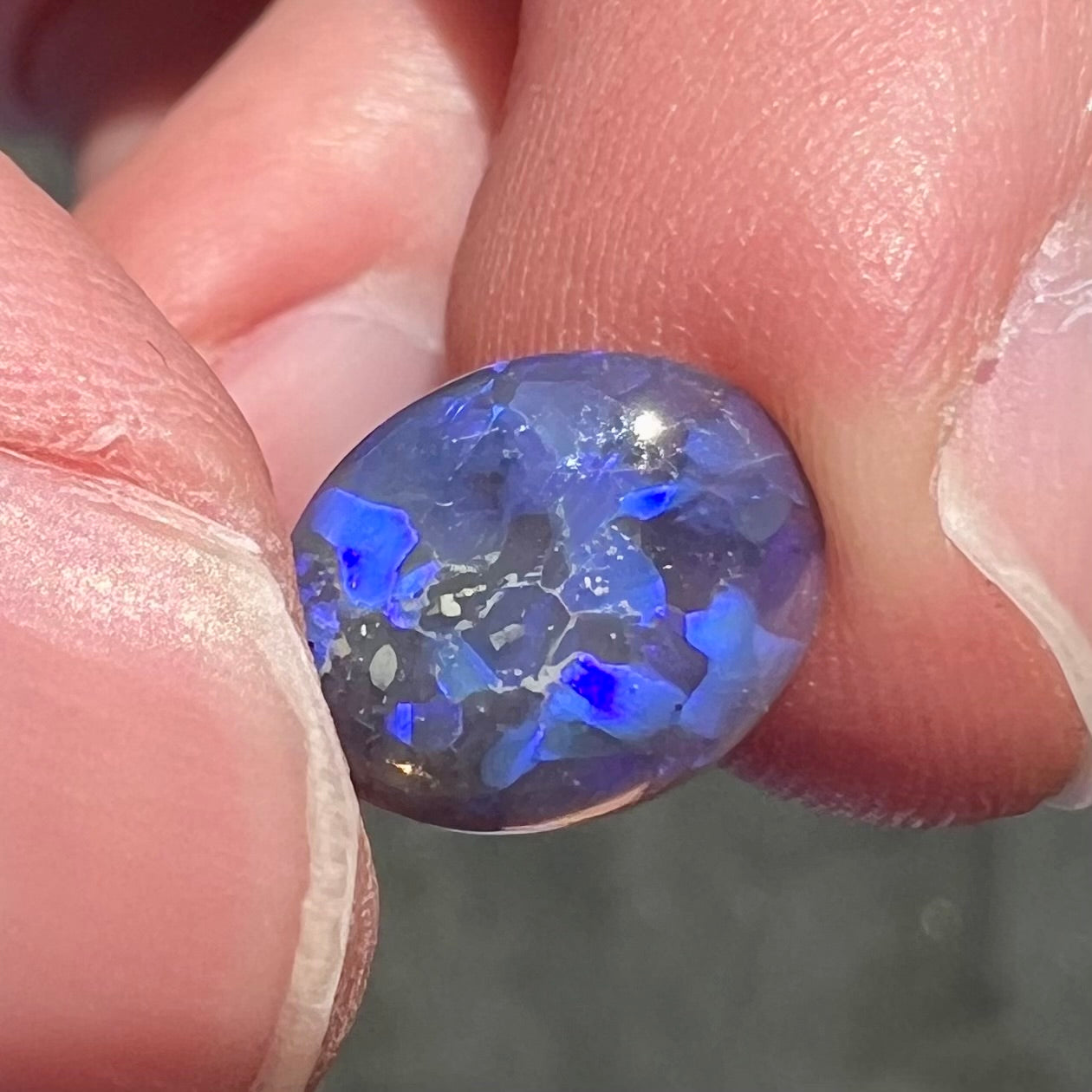 A loose, oval cabochon cut black crystal opal from Lightning Ridge, Australia.