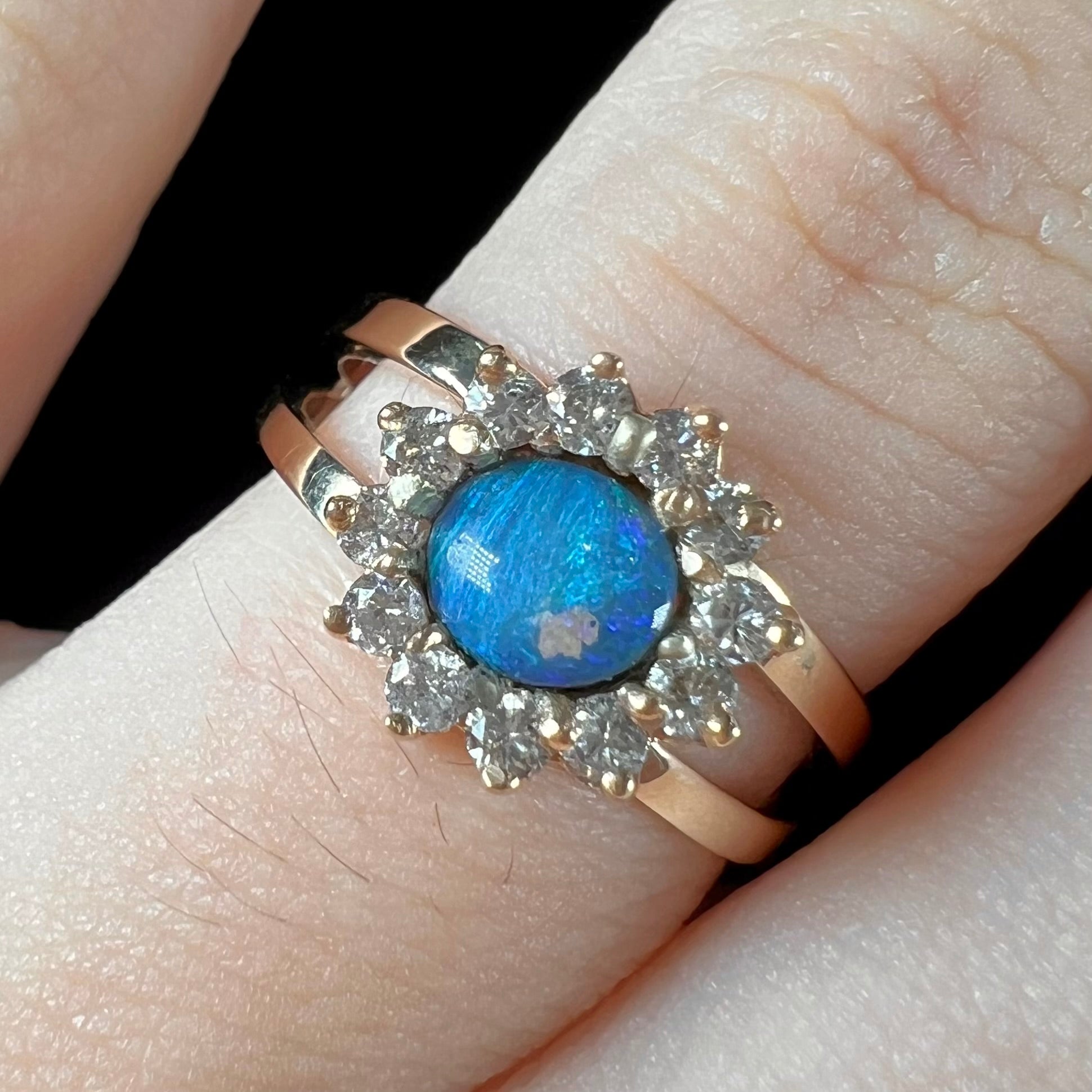 A ladies' round cut black opal and diamond halo ring.  The ring is yellow gold and has a split shank.