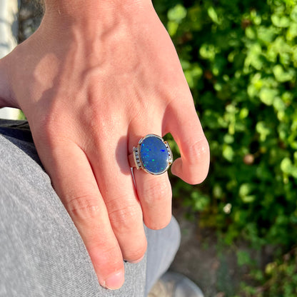 A large, unisex gold ring mounted with a half-bezel set black opal doublet and diamonds.