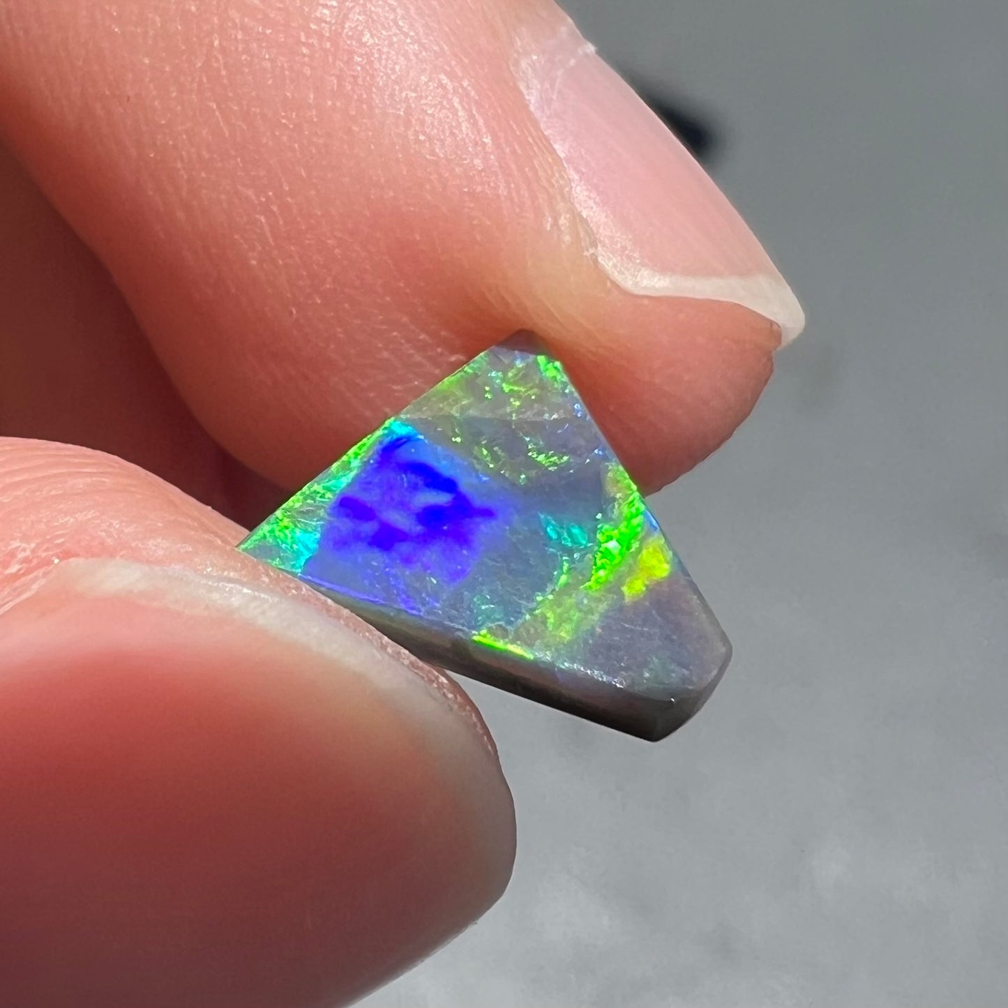 A loose, triangular shaped black opal from Lightning Ride, Australia.  The opal is predominantly green.