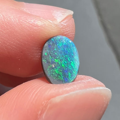 An oval cabochon cut loose Black opal stone from Lightning Ridge, Australia.