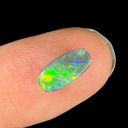 A loose, 1.37 carat black opal stone from Lightning Ridge, Australia.  The opal shows green and yellow colors.