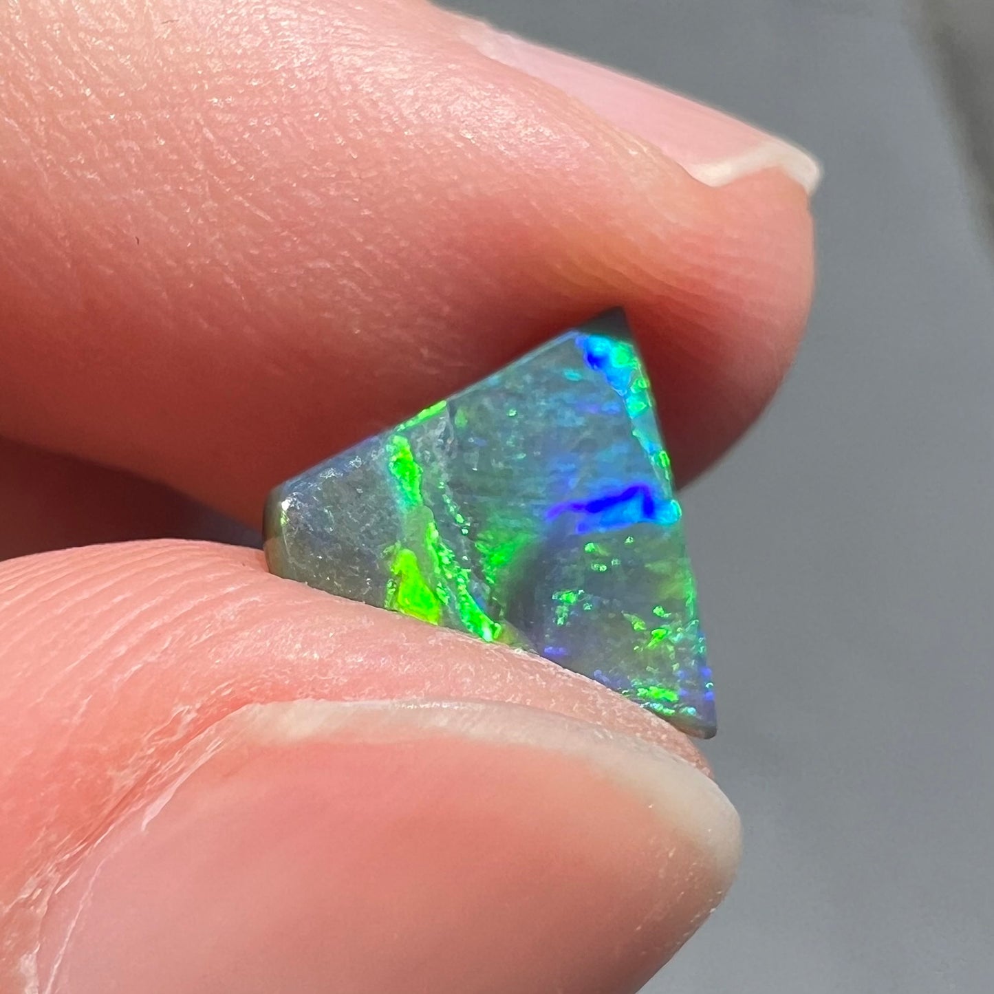 A loose, triangular shaped black opal from Lightning Ride, Australia.  The opal is predominantly green.