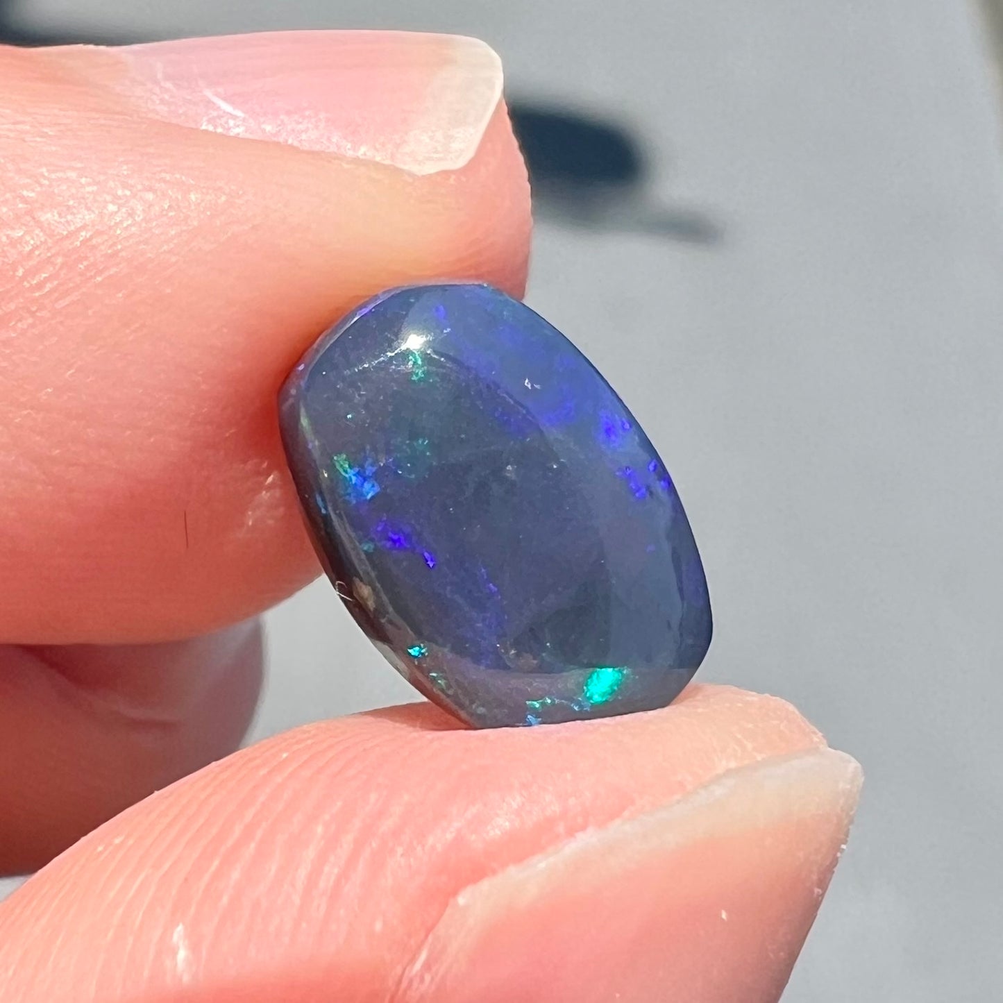 A loose Lightning Ridge black opal stone that shines colors of green, blue, and purple.