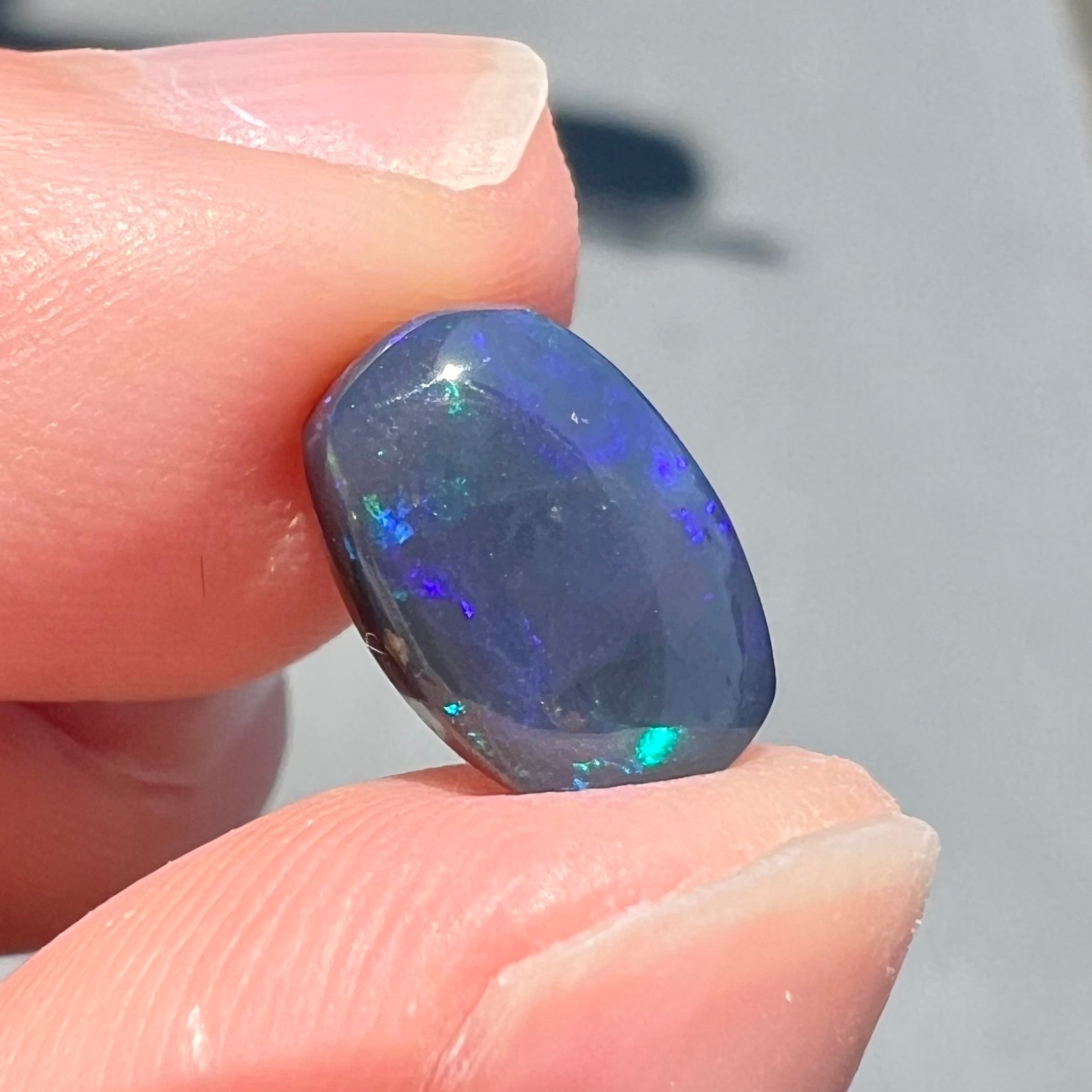 A loose Lightning Ridge black opal stone that shines colors of green, blue, and purple.