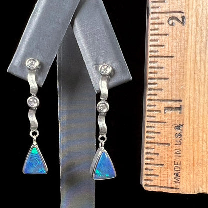 A pair of white gold earrings set with triangle cut natural black opals and round diamond accents.