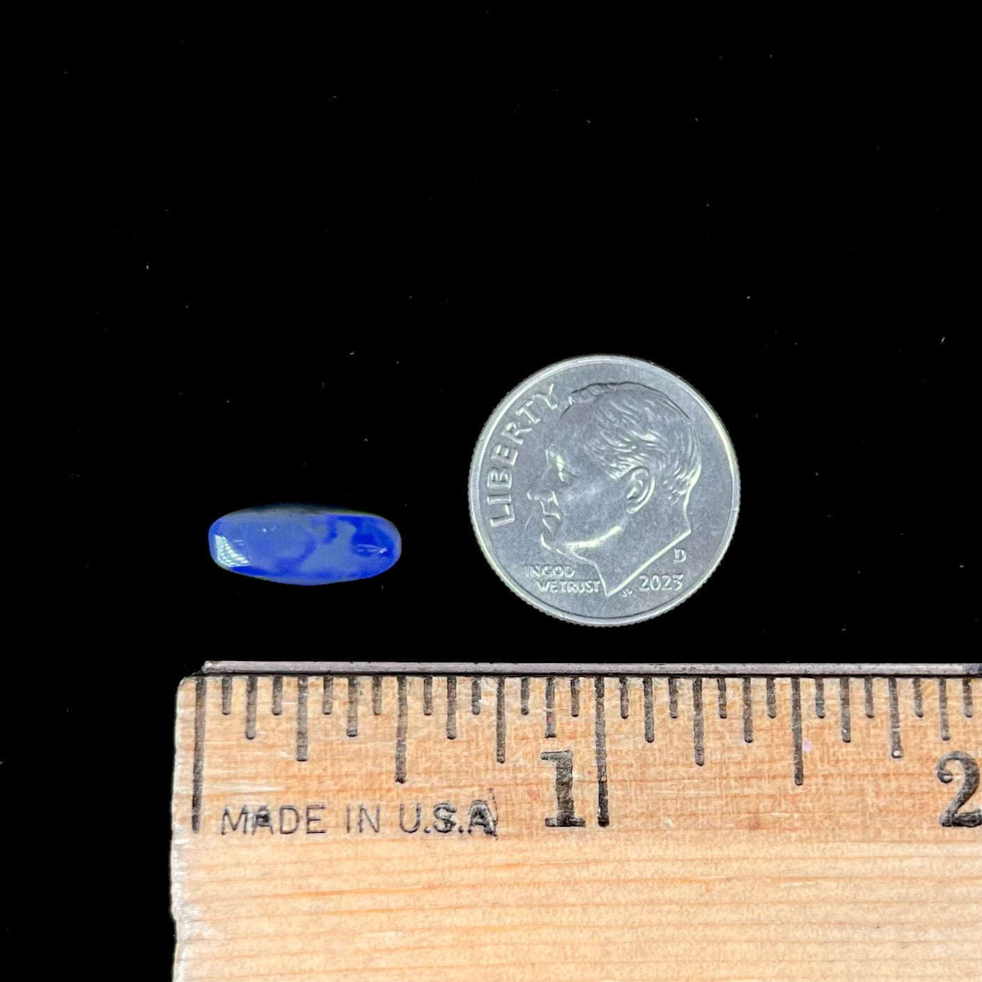 A loose, oval cabochon cut black opal stone that weighs 1.52 carats.  The opal plays blue colors.