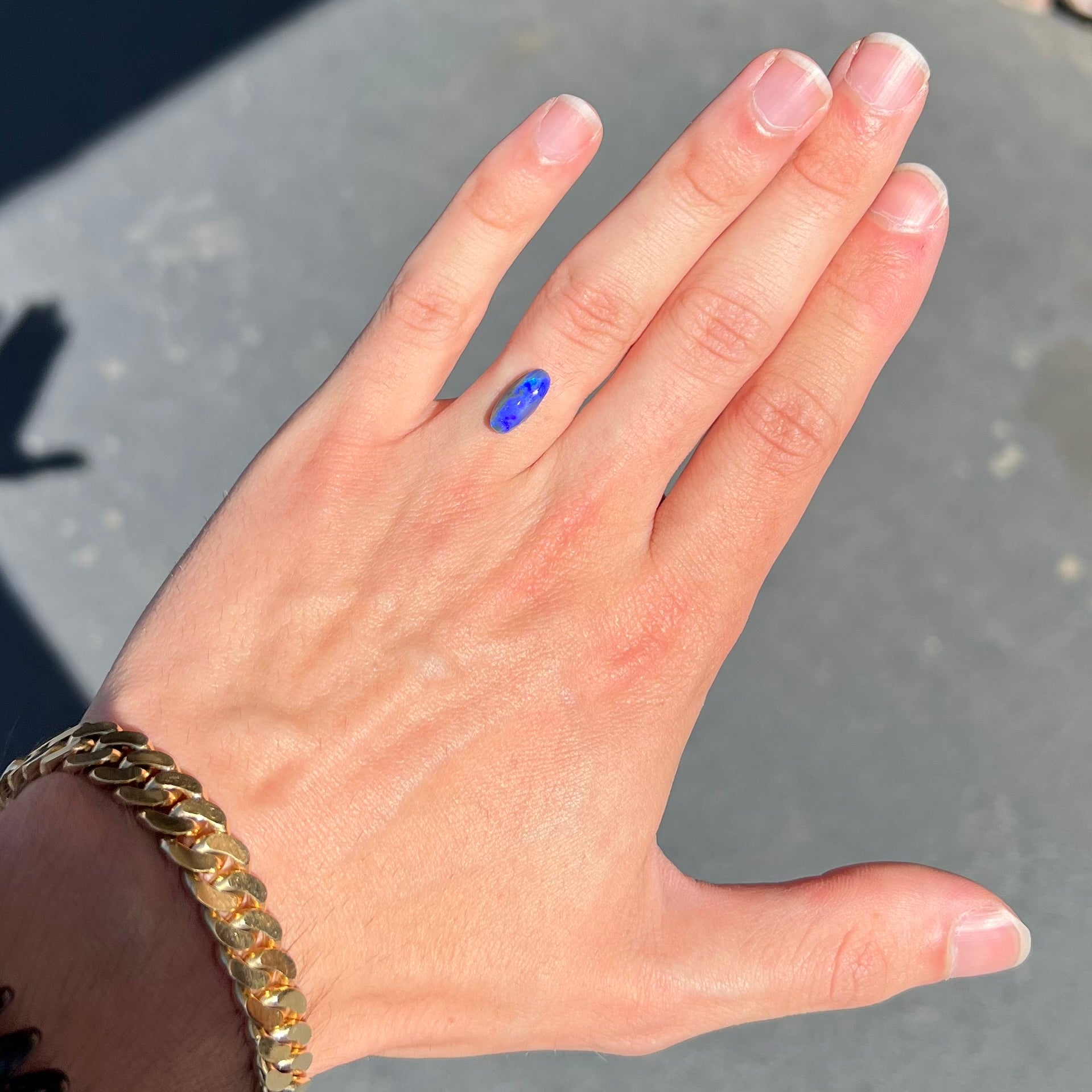 A loose, oval cabochon cut black opal stone that weighs 1.52 carats.  The opal plays blue colors.