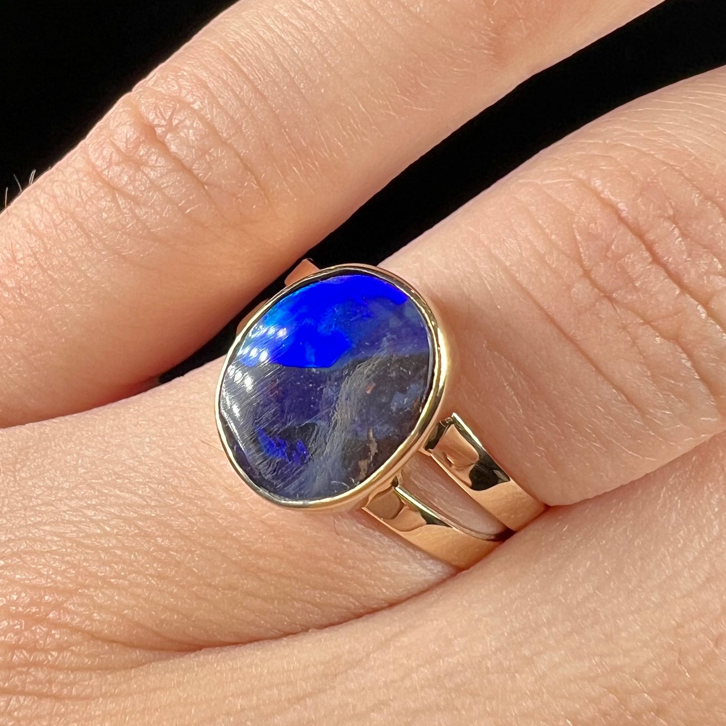 A ladies' split shank natural, Lightning Ridge, Australian black opal solitaire ring in yellow gold.