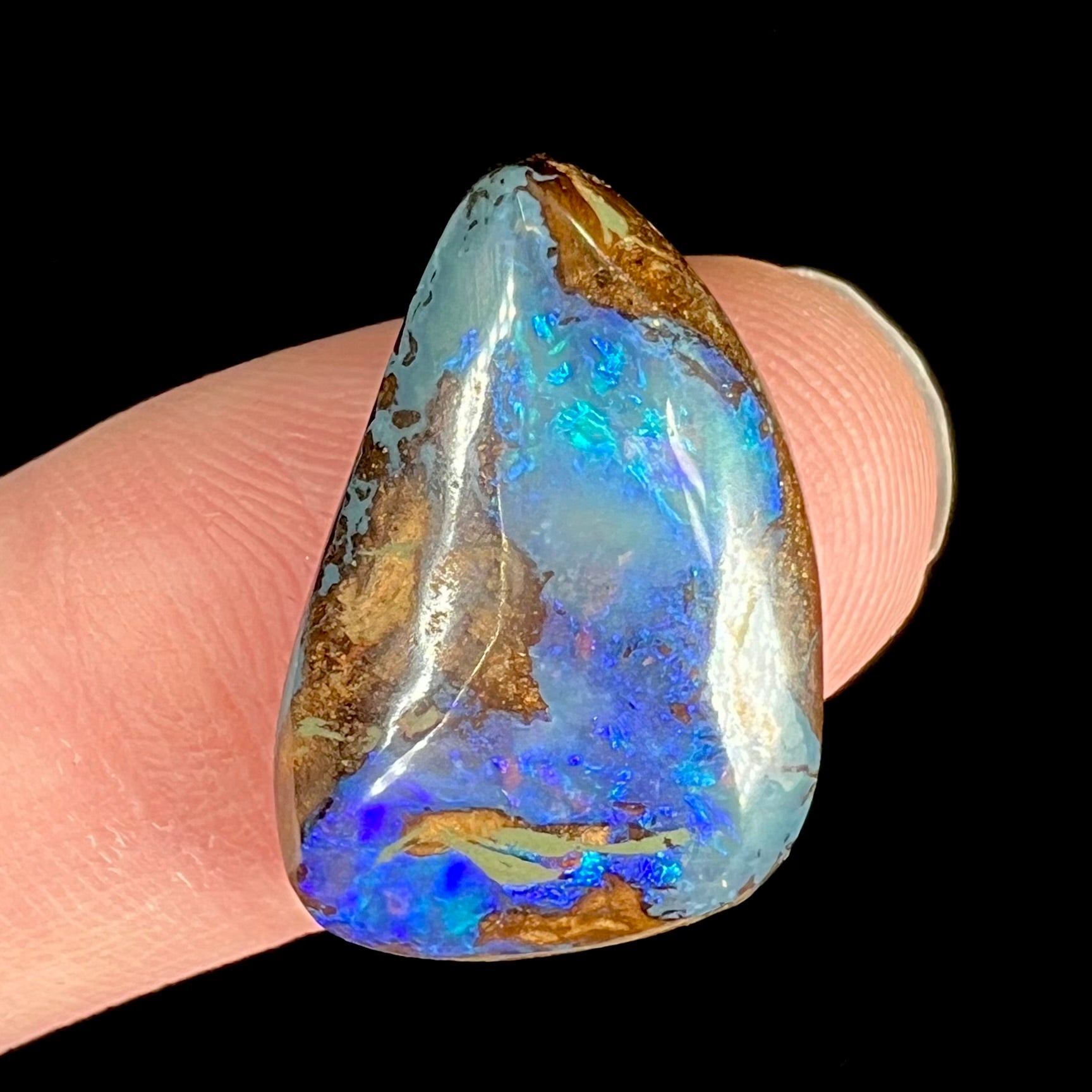 A freeform pear shaped boulder opal stone with blue color.