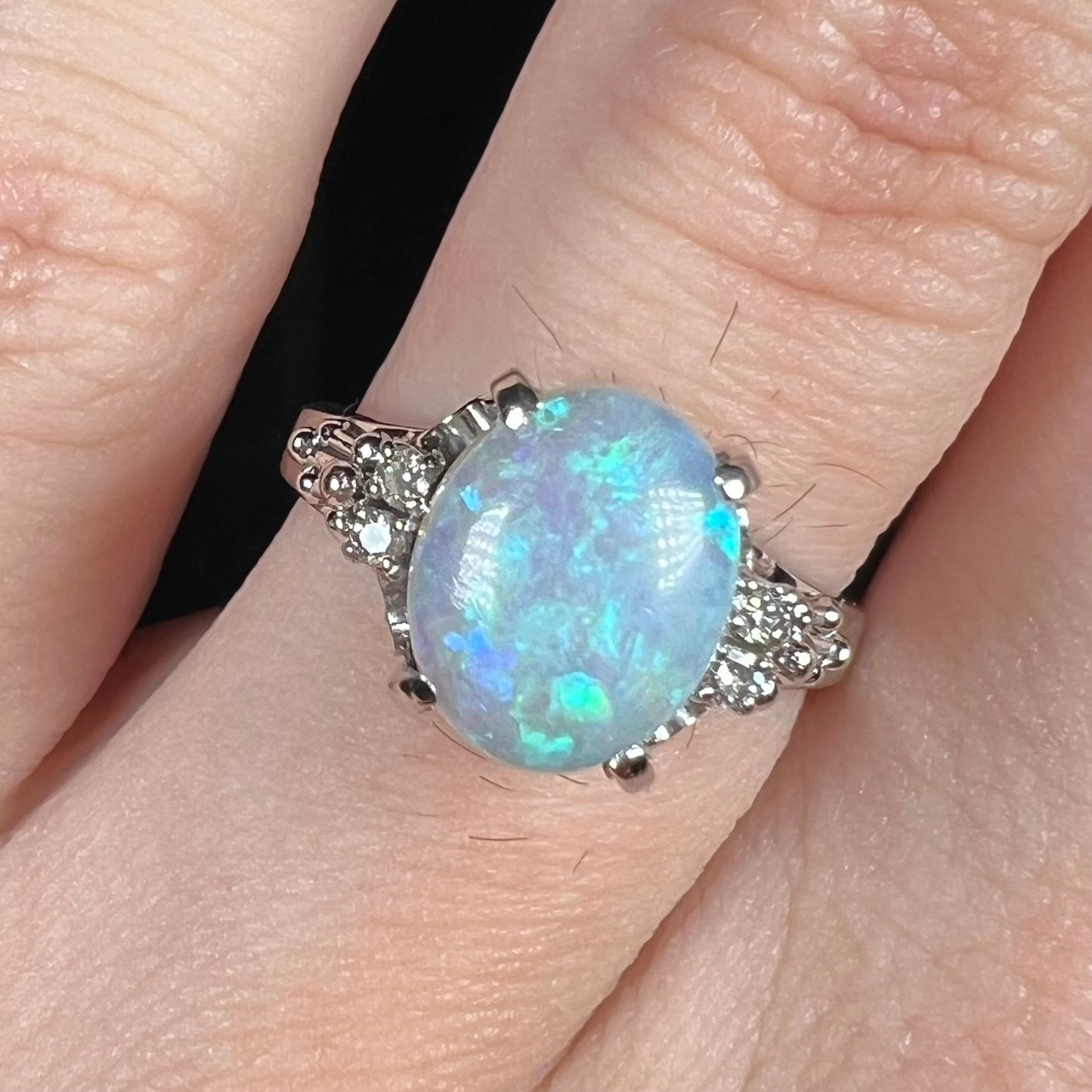 A platinum filigree ring mounted with a blue-green crystal opal and diamond accents.