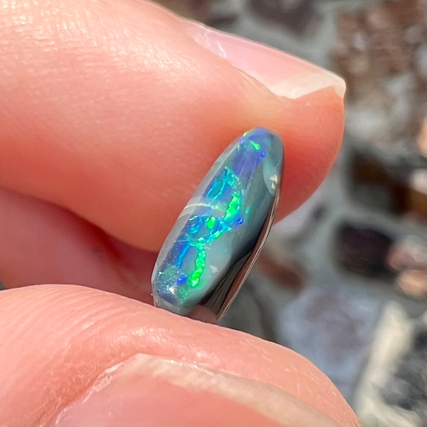 A loose, elongated oval cut black opal that has a green and blue cat's eye.