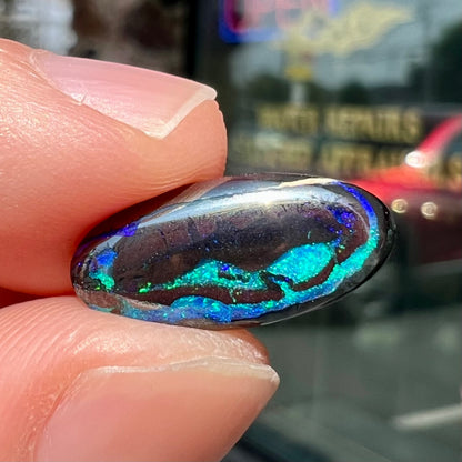 A loose, oval cabochon cut boulder opal stone.  The stone has bright blue and purple veins.