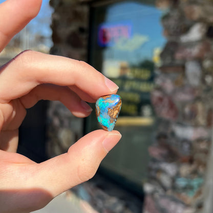 A freeform pear shaped boulder opal stone with blue color.