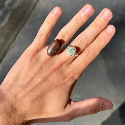 An oval cabochon cut boulder opal stone with green, blue, purple, and red play of color.