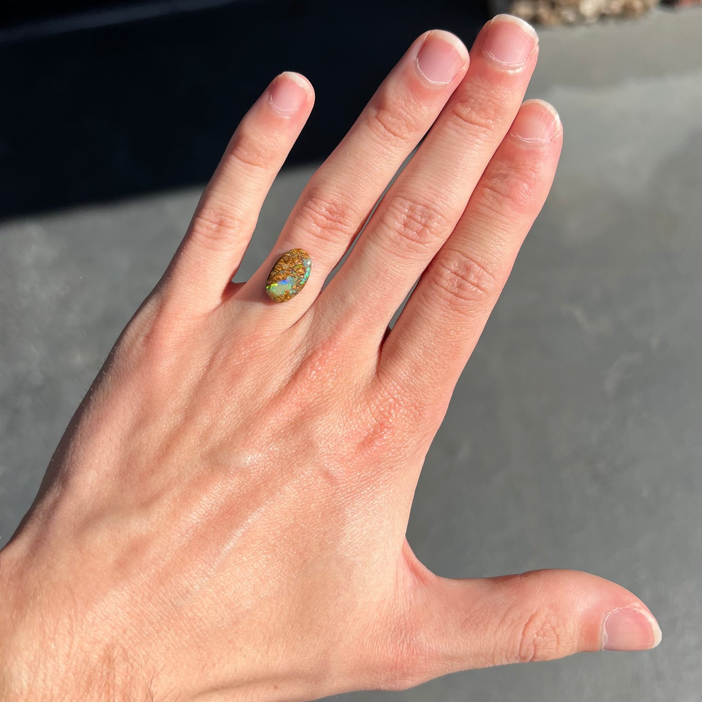 A loose, oval cabochon cut Koroit boulder opal with green fire.