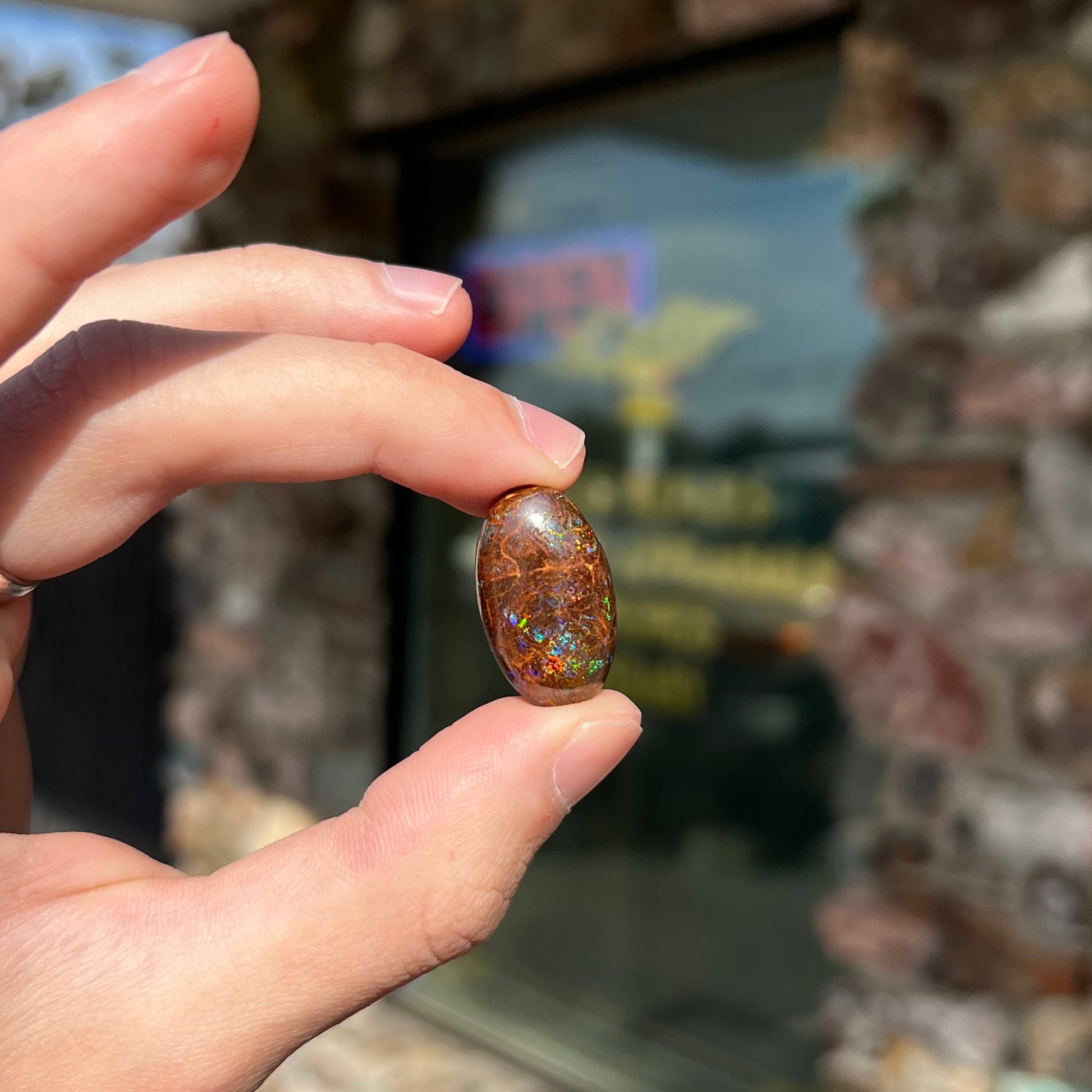 An oval cabochon cut boulder opal stone with green, blue, purple, and red play of color.