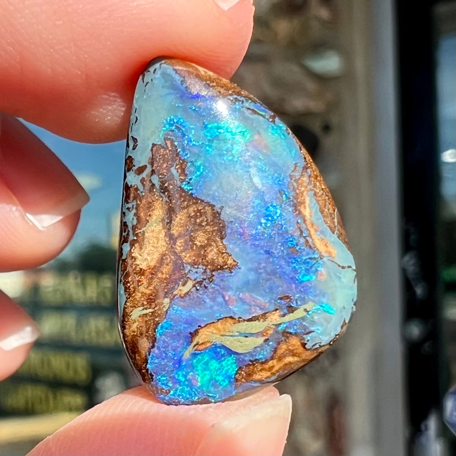 A freeform pear shaped boulder opal stone with blue color.