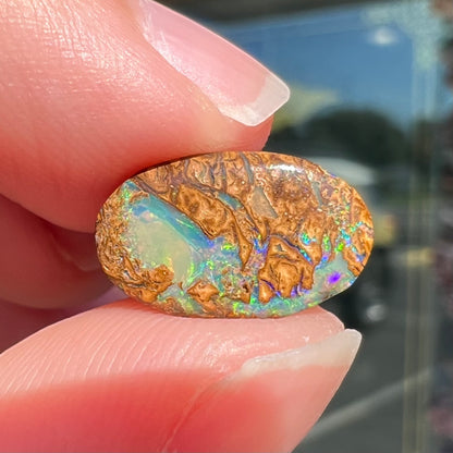 A loose, oval cabochon cut Koroit boulder opal with green fire.