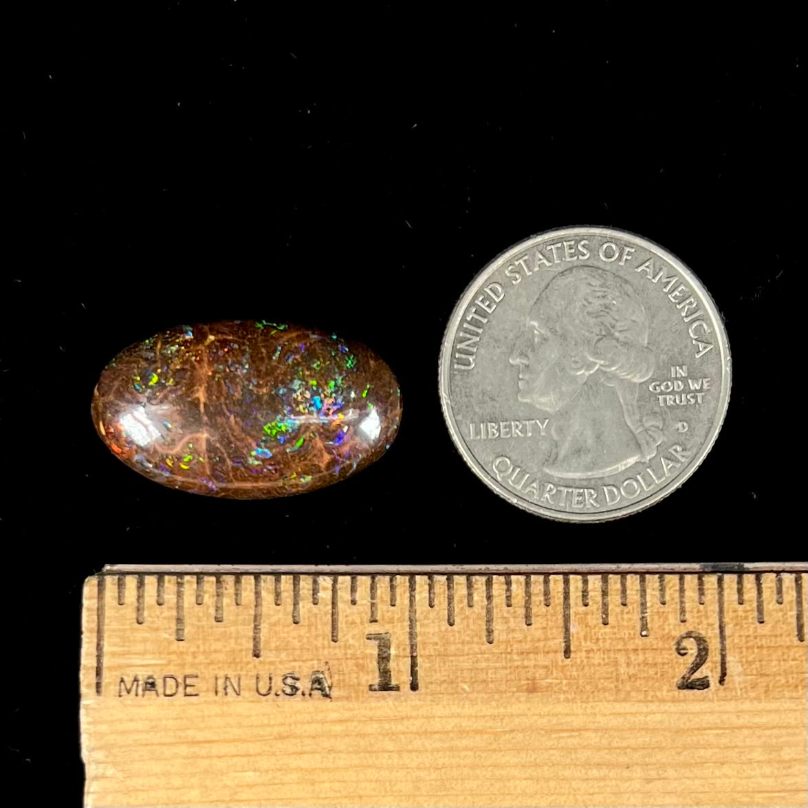 An oval cabochon cut boulder opal stone with green, blue, purple, and red play of color.