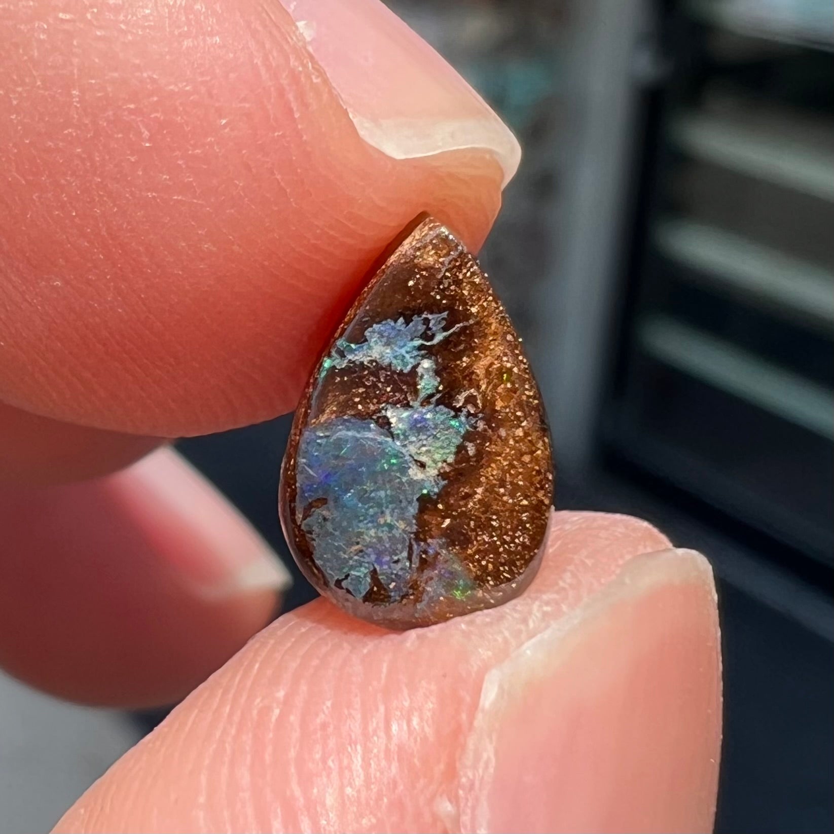 A loose, pear shaped boulder opal stone that flashes colors of green and blue.