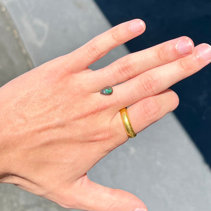 A loose, pear shaped boulder opal stone that flashes colors of green and blue.