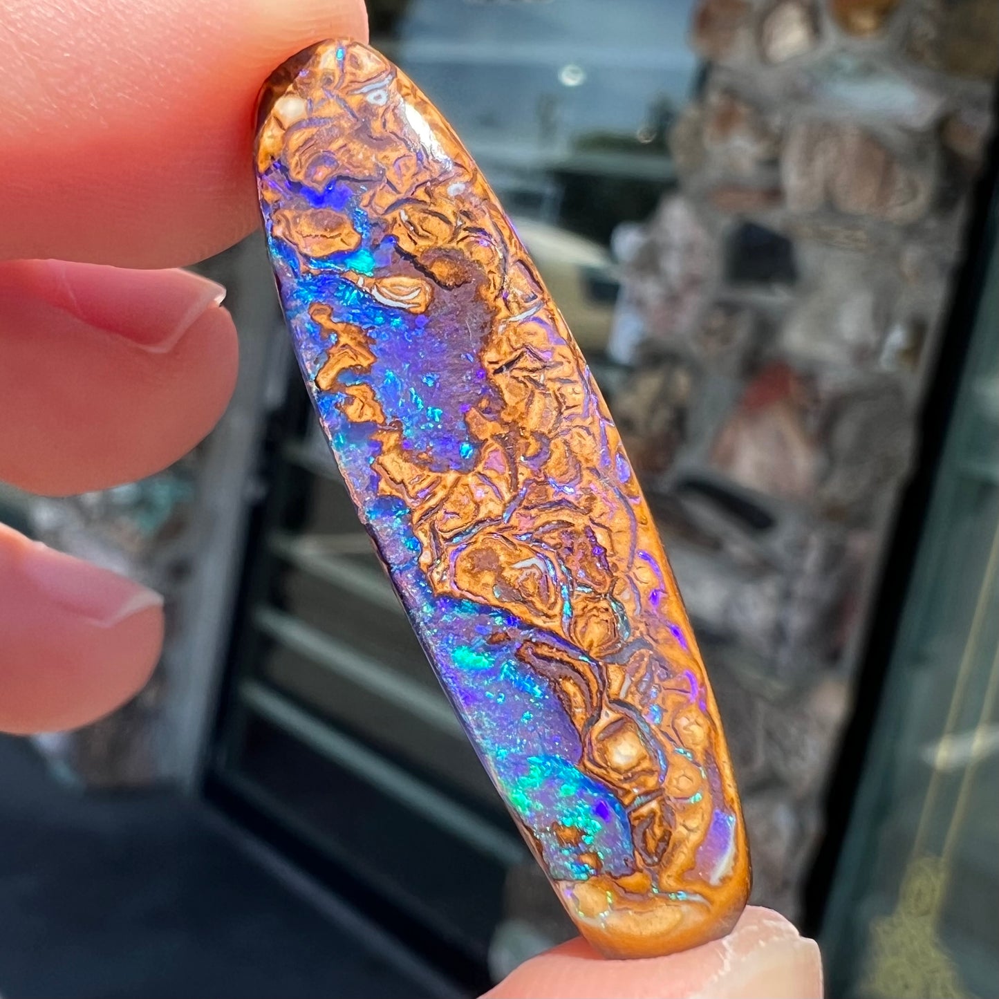 A polished boulder opal stone from Koroit, Australia.  The stone has blue and purple veins.