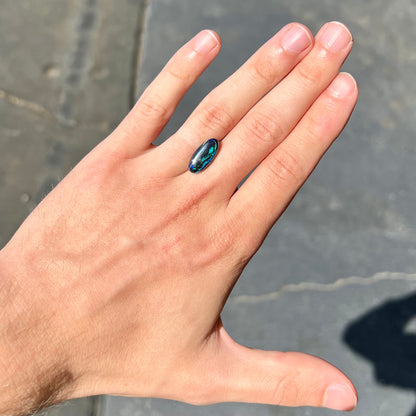 A loose, oval cabochon cut boulder opal stone.  The stone has bright blue and purple veins.