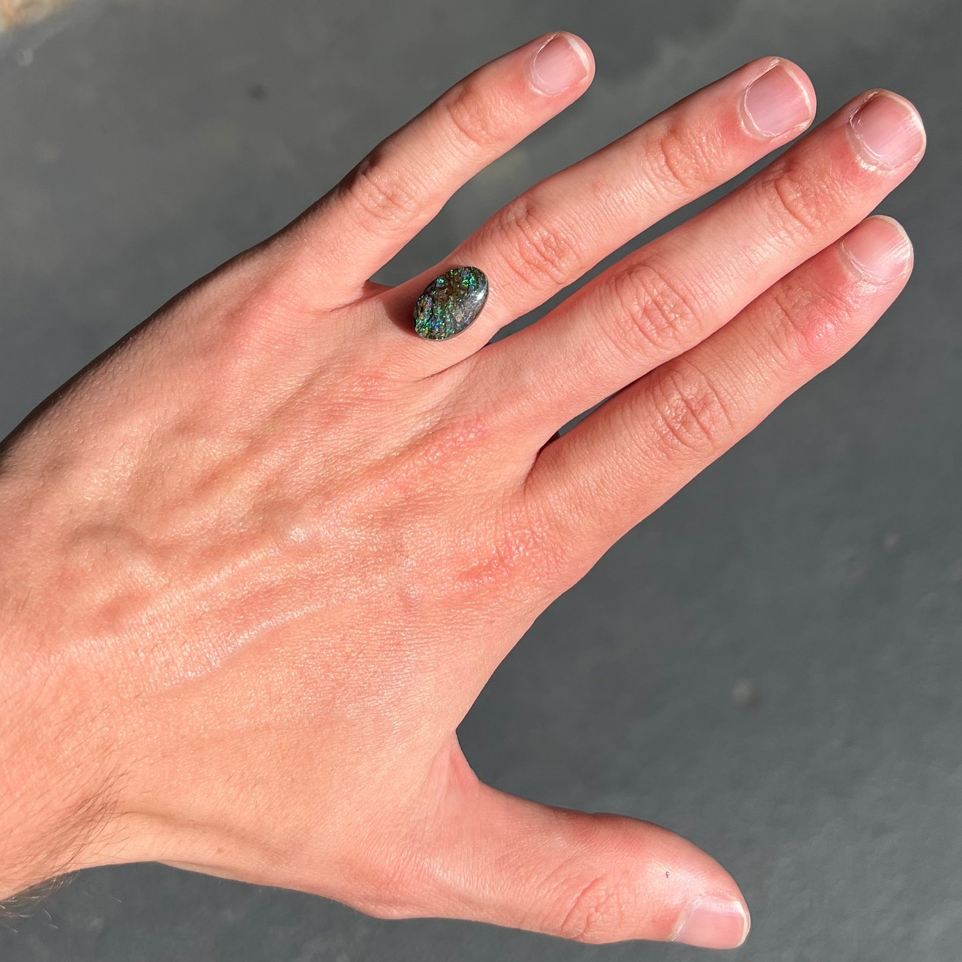 A loose, oval cabochon cut matrix boulder opal stone from Koroit, Australia.  The opal shines with green and blue colors.