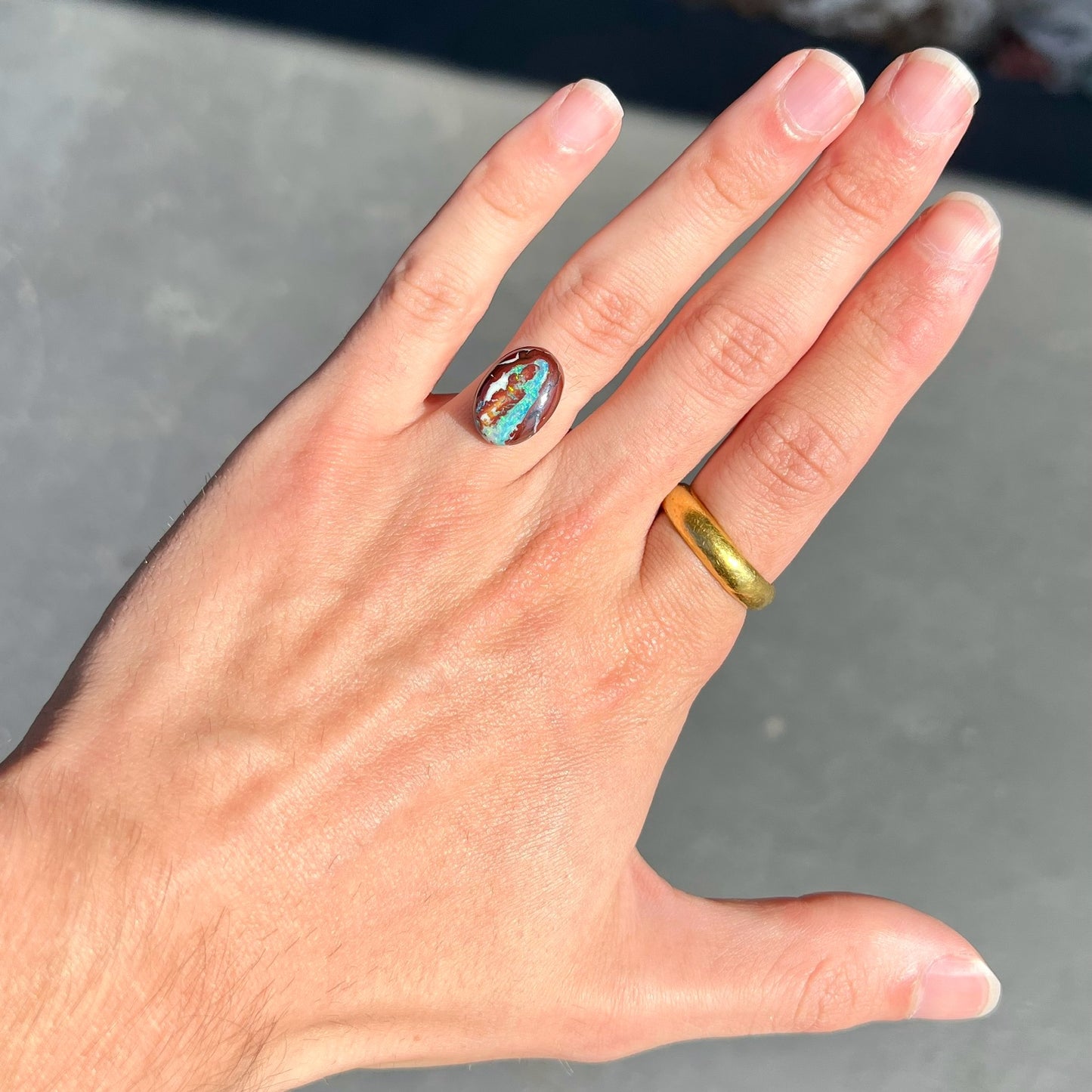 A loose, oval cabochon cut boulder opal stone from Australia.  The opal has blue and green veins in an ironstone matrix.