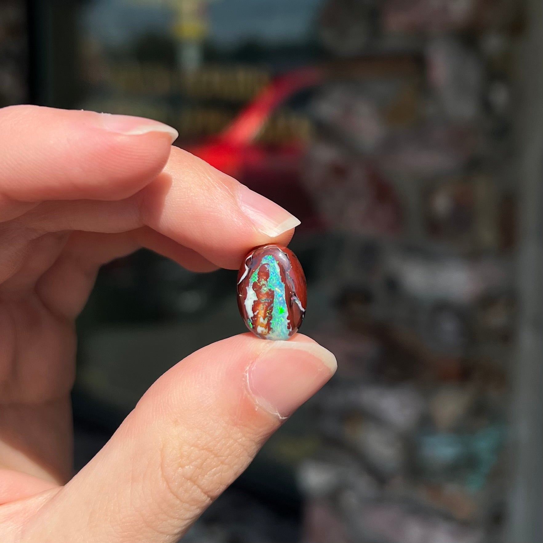 A loose, oval cabochon cut boulder opal stone from Australia.  The opal has blue and green veins in an ironstone matrix.