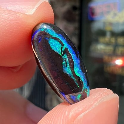 A loose, oval cabochon cut boulder opal stone.  The stone has bright blue and purple veins.