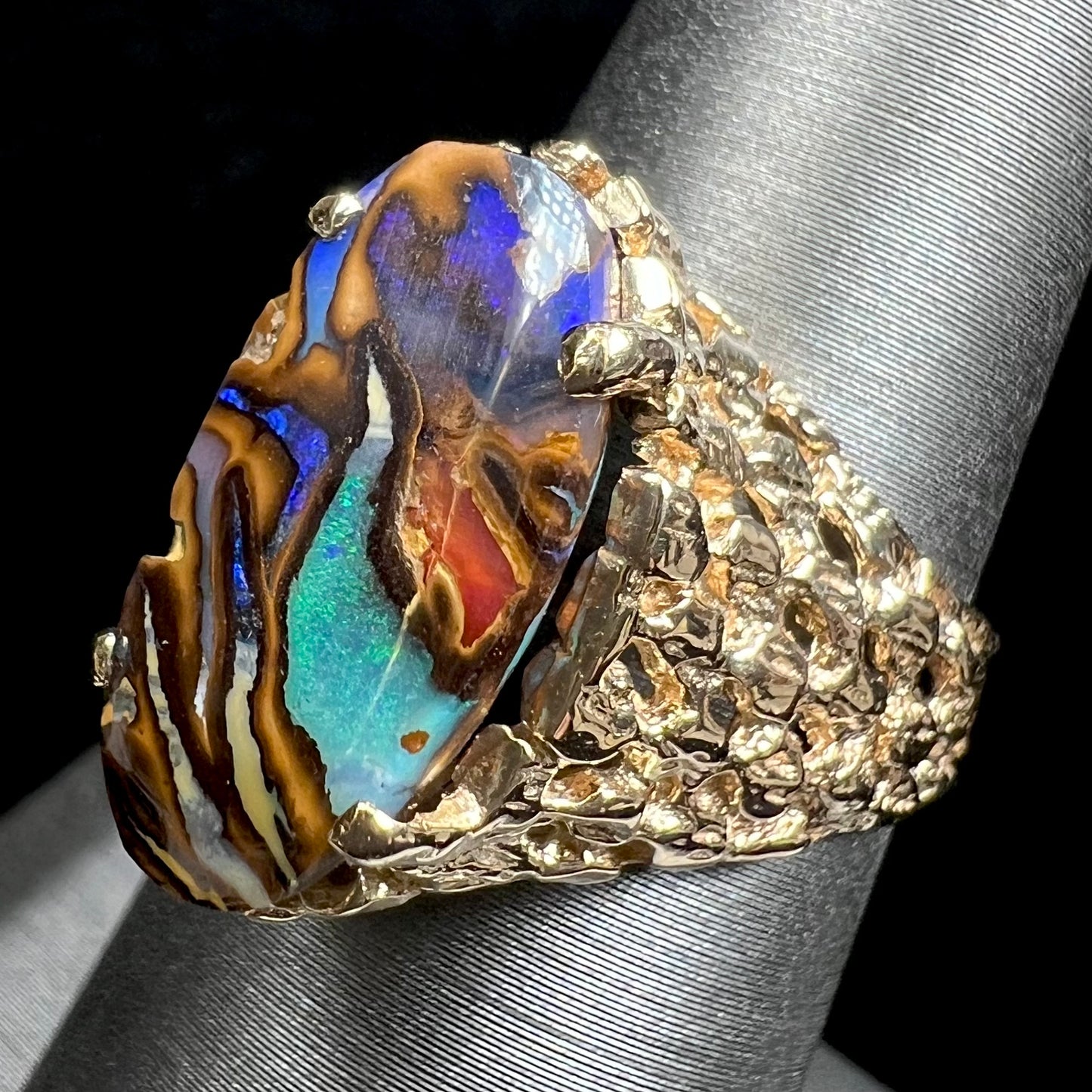 A yellow gold solitaire ring mounted with a Koroit boulder opal stone that shows the picture of a peacock.