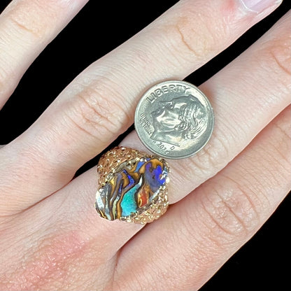 A yellow gold solitaire ring mounted with a Koroit boulder opal stone that shows the picture of a peacock.