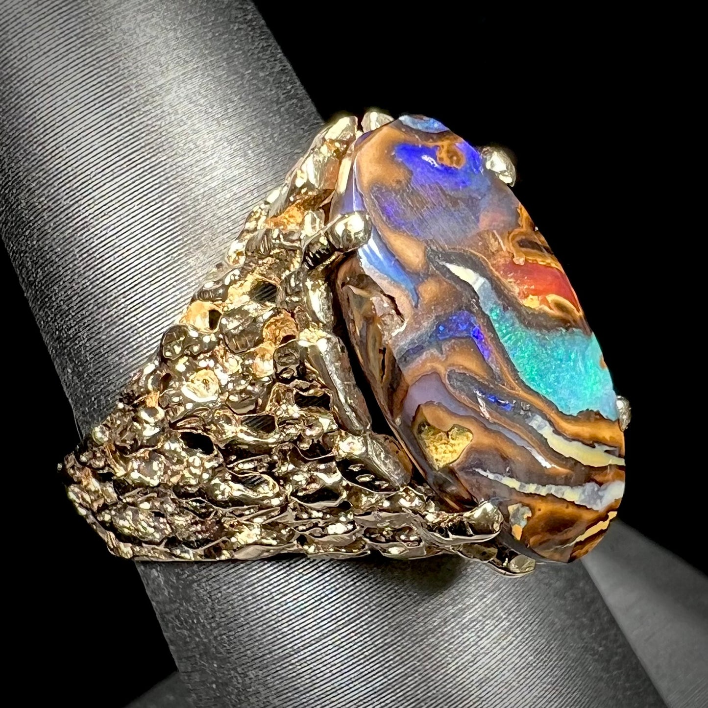 A yellow gold solitaire ring mounted with a Koroit boulder opal stone that shows the picture of a peacock.