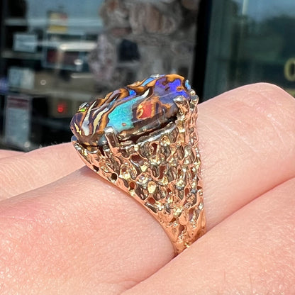 A yellow gold solitaire ring mounted with a Koroit boulder opal stone that shows the picture of a peacock.