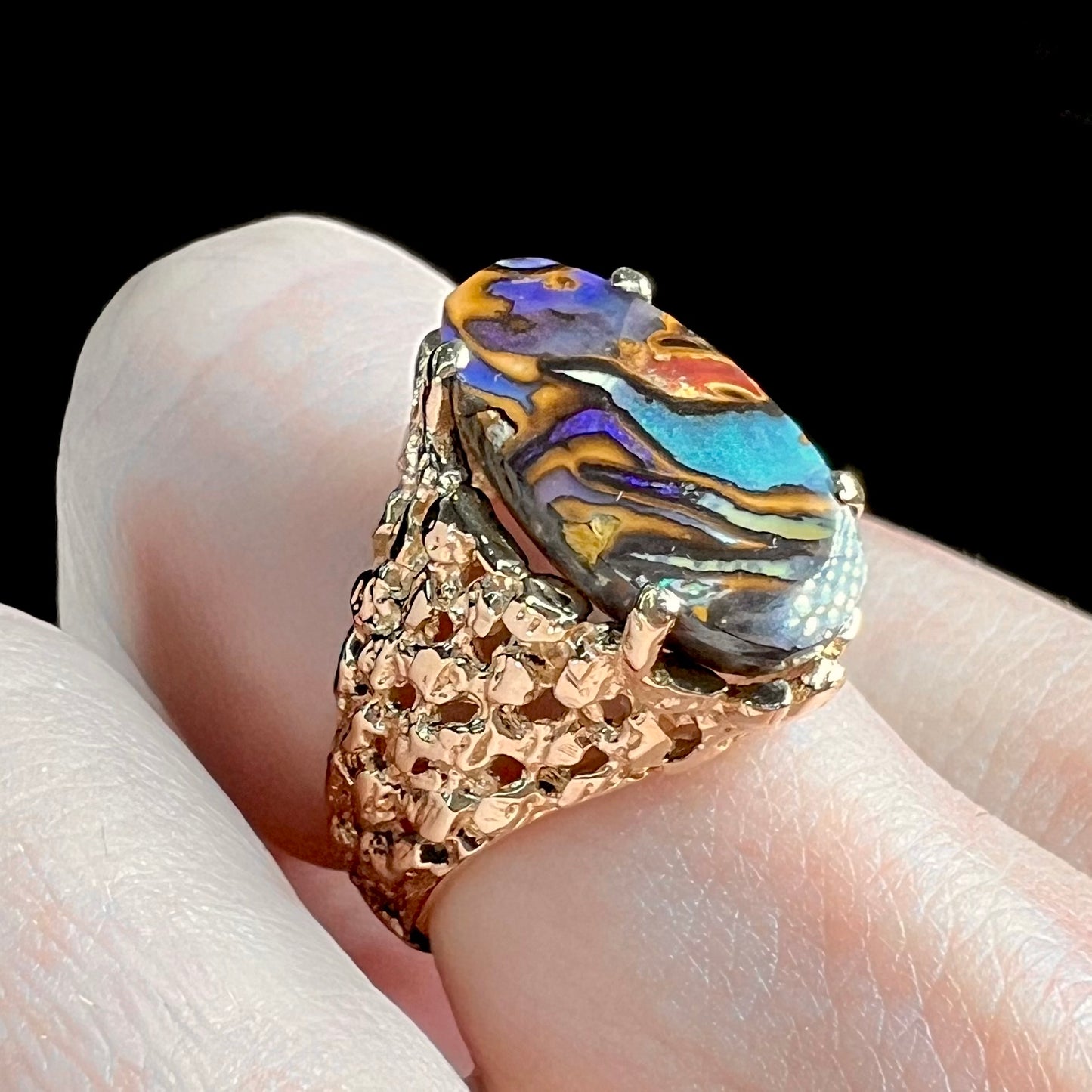 A yellow gold solitaire ring mounted with a Koroit boulder opal stone that shows the picture of a peacock.