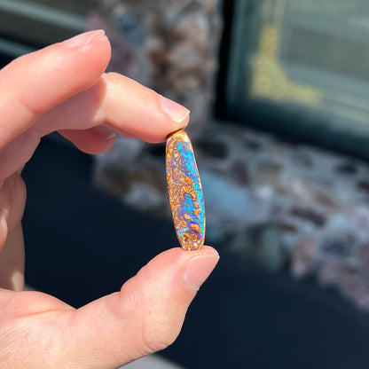 A polished boulder opal stone from Koroit, Australia.  The stone has blue and purple veins.