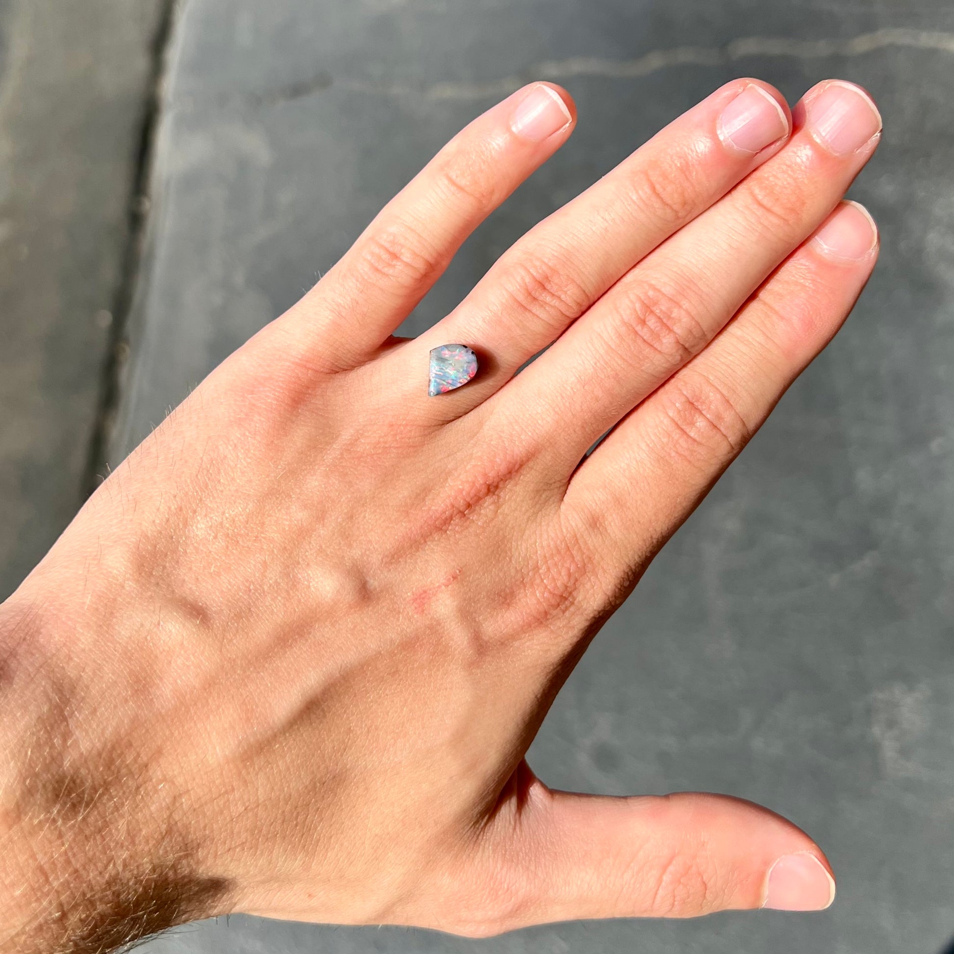 A freeform shaped boulder opal stone with red and blue color play.