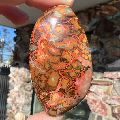 A polished boulder opal stone from Koroit, Australia.  The stone has been drilled with a bead hole.