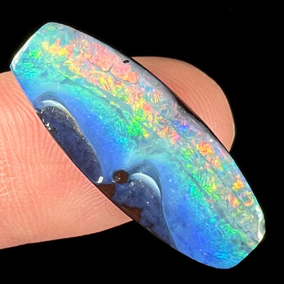 A barrel shaped boulder opal gemstone with a rainbow of colors.