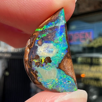 A loose, freeform shaped boulder opal with green and blue multicolor fire from Australia.