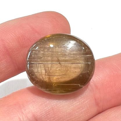 A loose, golden brown cat's eye dravite tourmaline gemstone.  The stone is cut into an oval shaped cabochon.