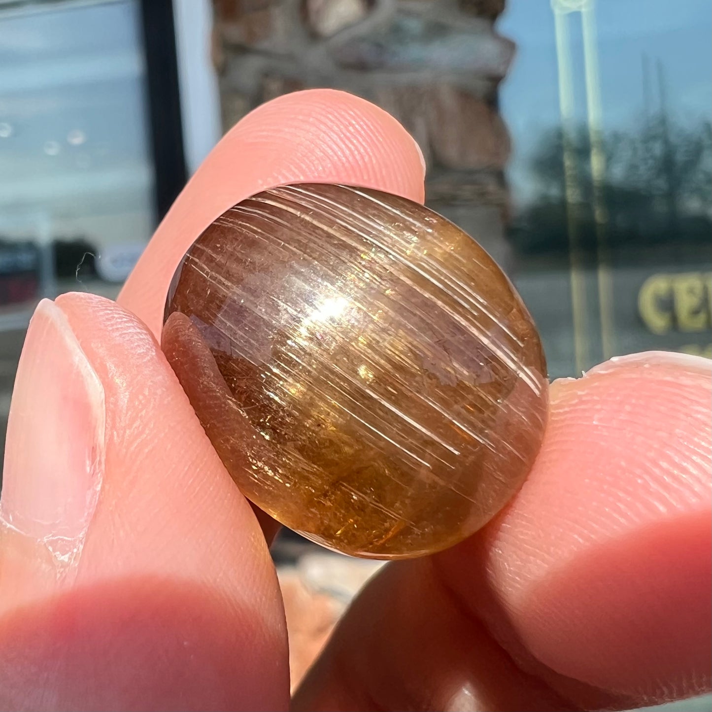 A loose, golden brown cat's eye dravite tourmaline gemstone.  The stone is cut into an oval shaped cabochon.