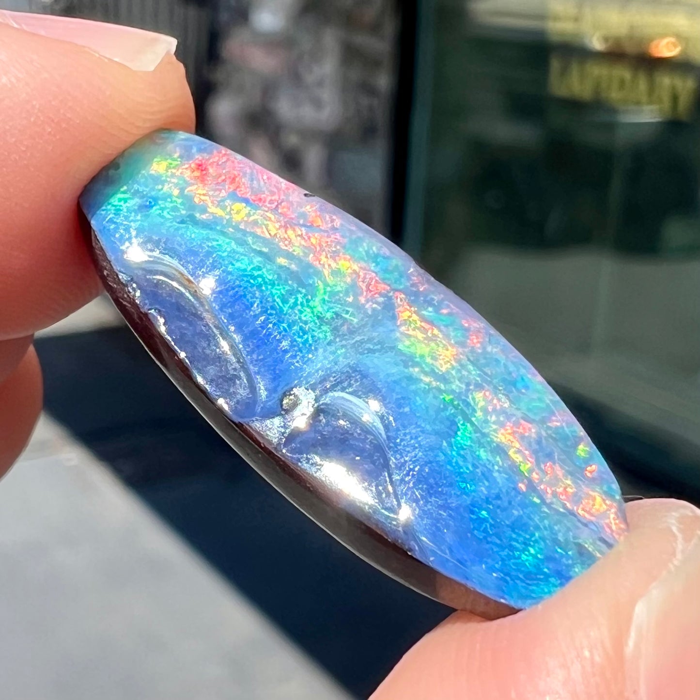 A barrel shaped boulder opal gemstone with a rainbow of colors.