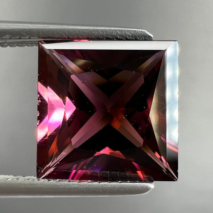 A loose, faceted princess cut tourmaline gemstone.  The stone is a burgundy purple color.