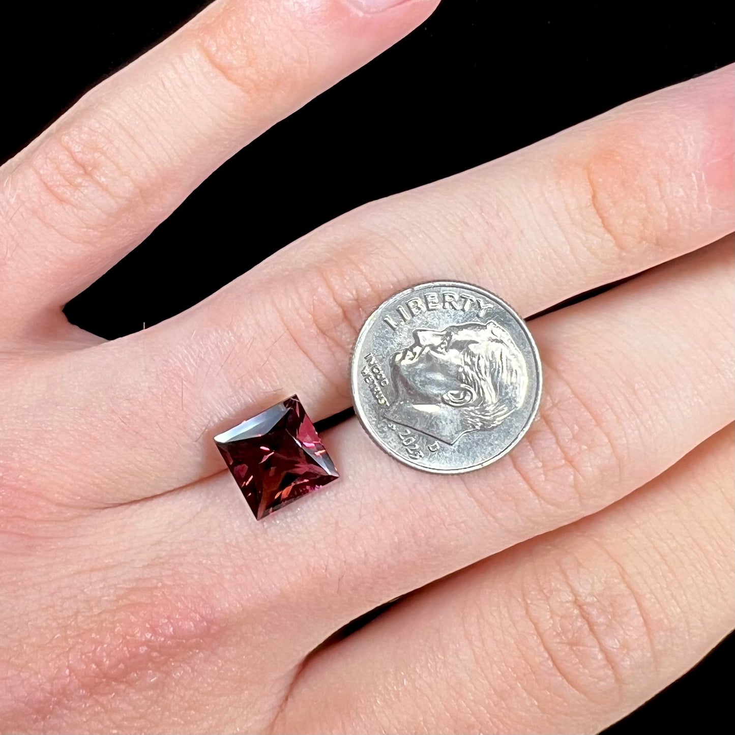 A loose, faceted princess cut tourmaline gemstone.  The stone is a burgundy purple color.