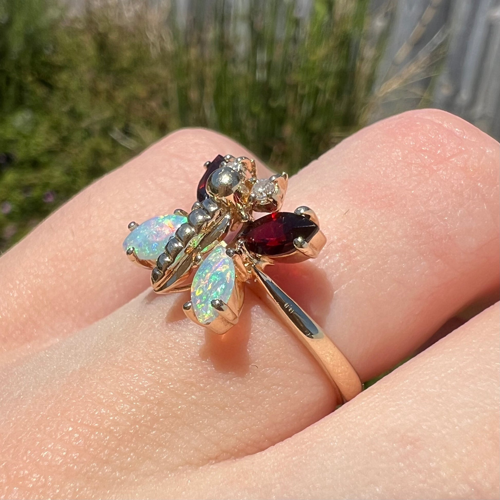 A yellow gold butterfly ring mounted with marquise cut garnets and opals and round diamond accents.