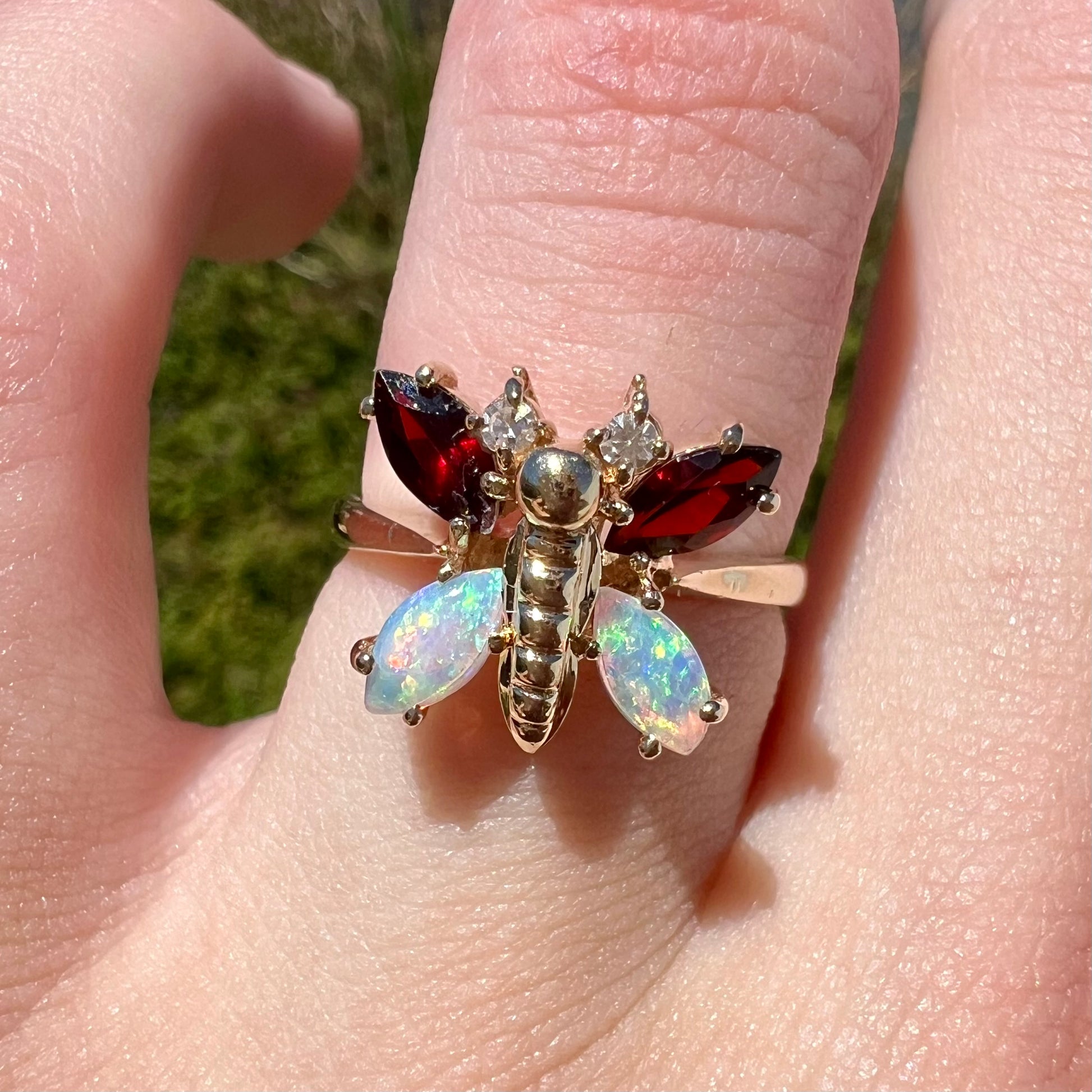 A yellow gold butterfly ring mounted with marquise cut garnets and opals and round diamond accents.