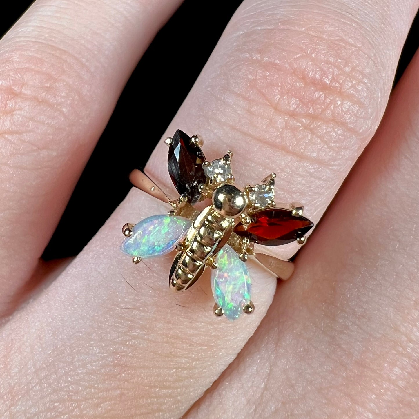 A yellow gold butterfly ring mounted with marquise cut garnets and opals and round diamond accents.